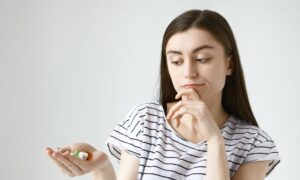 Mujer pensativa observando medicamentos en su mano, pensando si es seguro tomar estos tratamientos para la ovulación