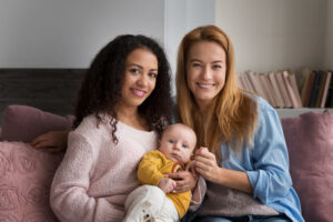 Pareja de mujeres sonríe junto a su bebé, representando la maternidad compartida posible gracias al Método ROPA.